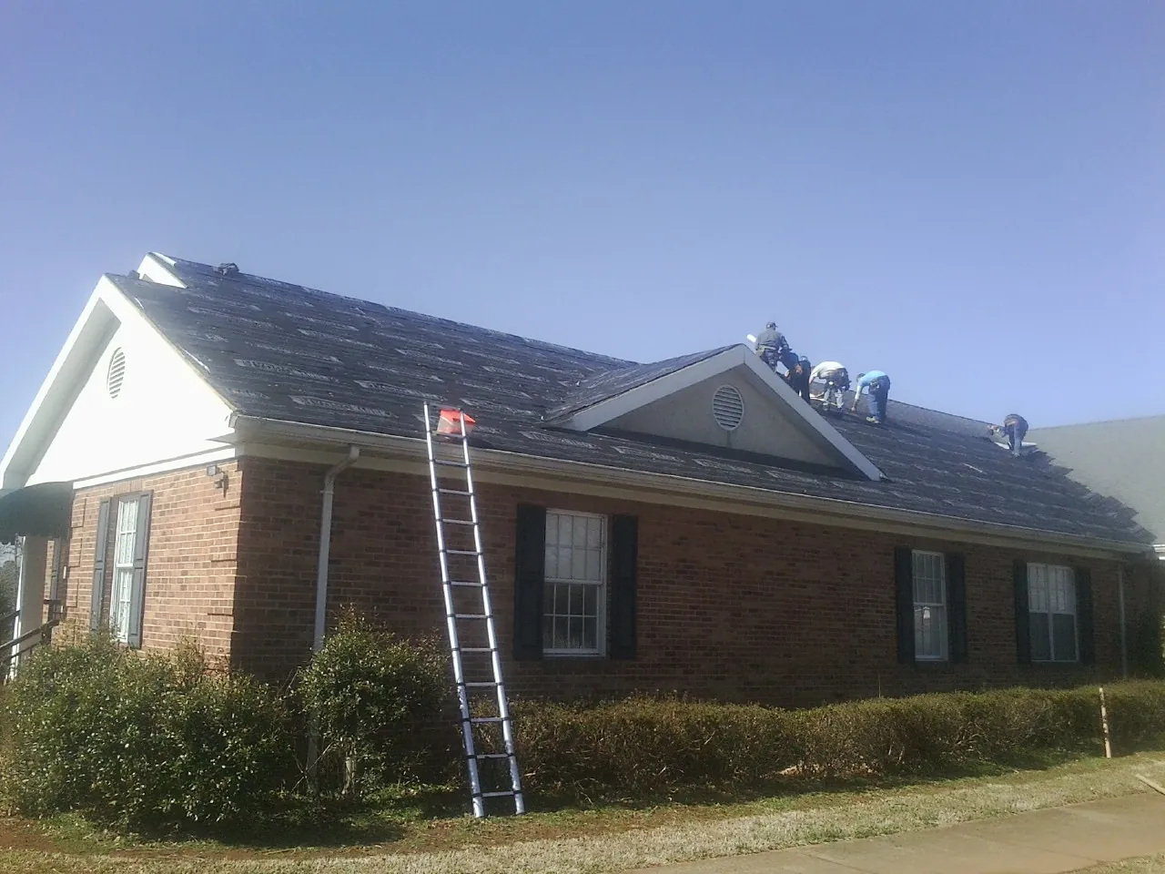 Crew tearing shingles off a brick ranch roof with a ladder set — Emergency Roof Repair work by our crew in Fishing Creek