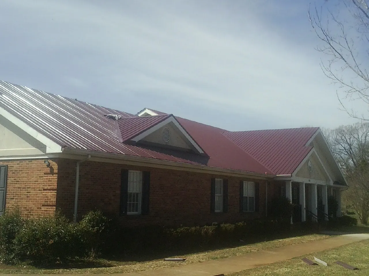 Red metal roof with gabled entries on a long brick building, from a Hail Damage Roof Repair job in Fishing Creek