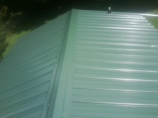 New green metal panels meeting at the ridge of a roof — Flat Roof Repair work by our crew in Fishing Creek