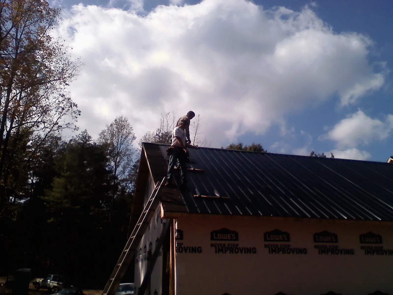 Roofer fastening dark metal panels high against a cloudy sky, from a Roof Inspection job in Fishing Creek