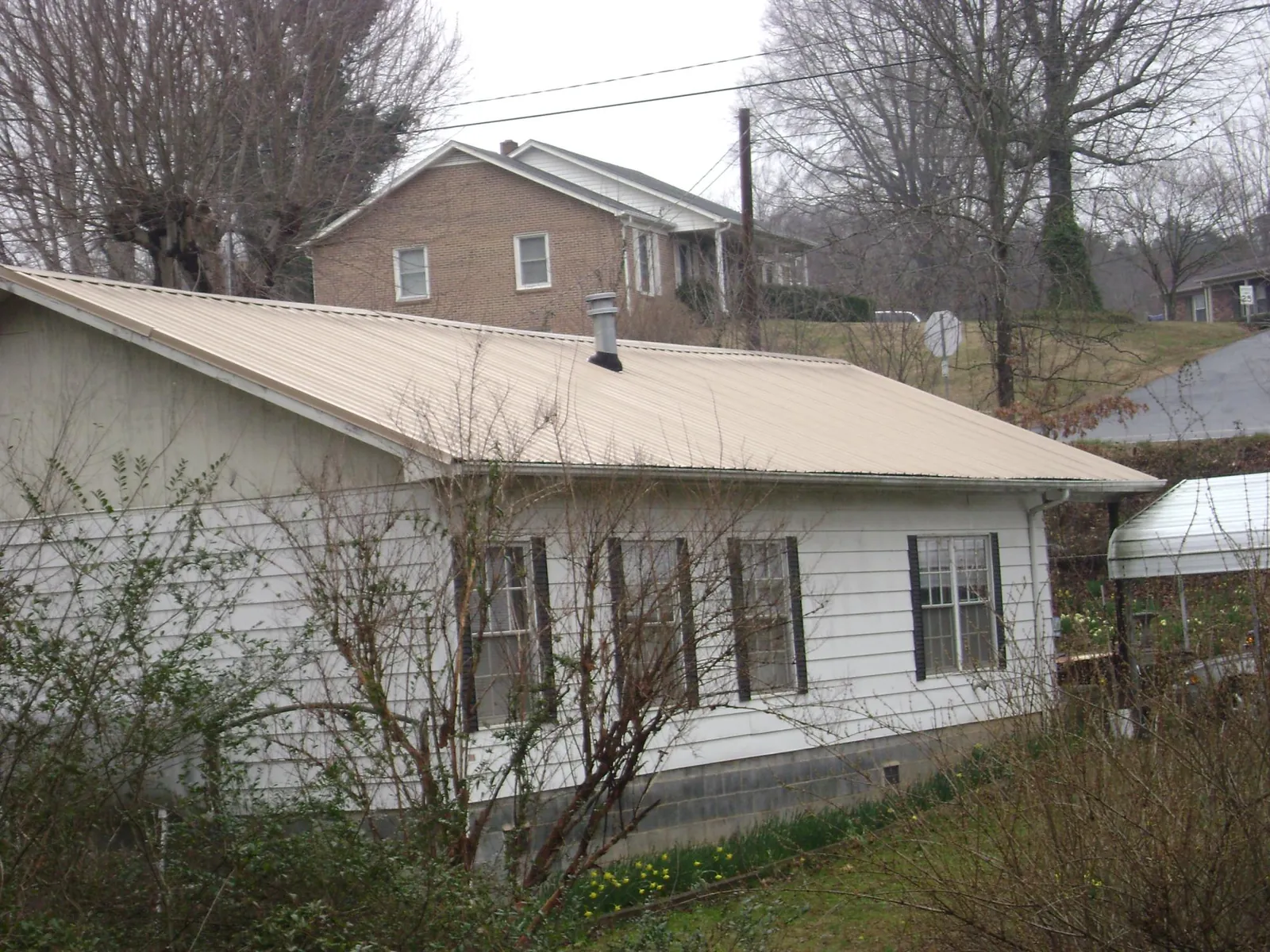 Tan metal roof on a white sided house set into a hillside — Commercial Roofing by Roofing Brothers in Fishing Creek