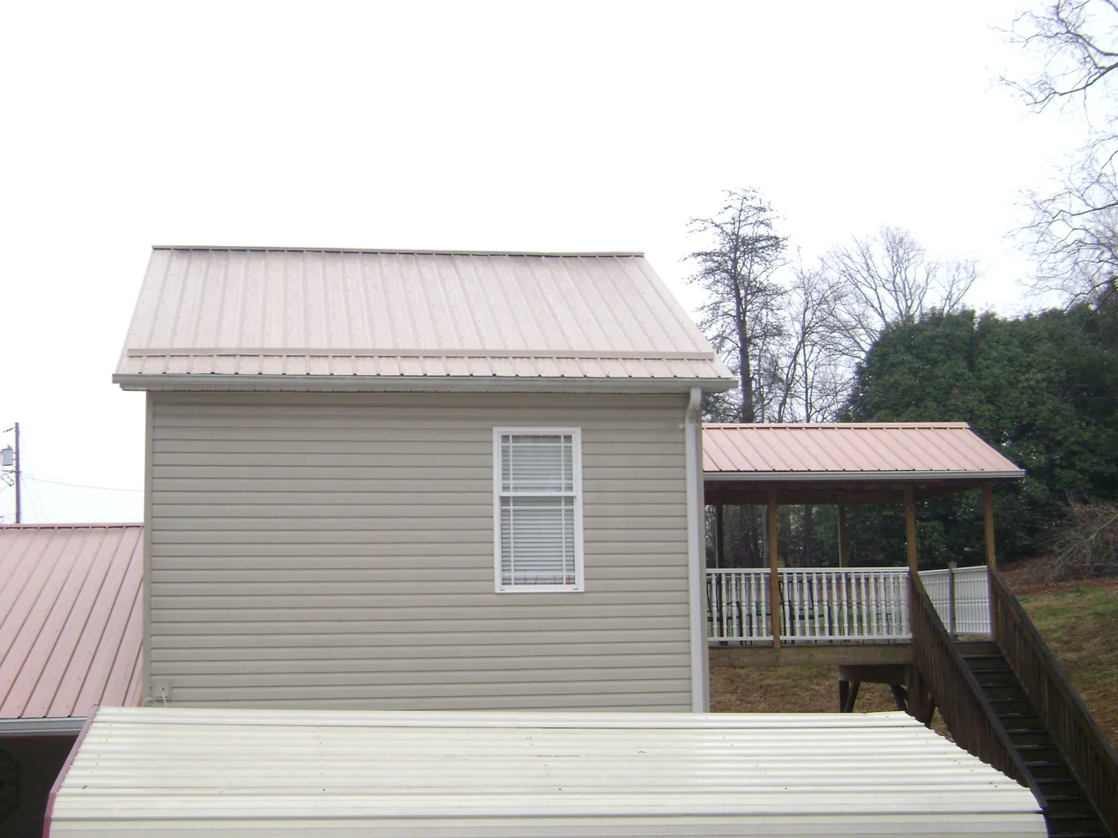 Tan metal roofs on a two story addition and attached porch, from a Roof Replacement job in Fishing Creek
